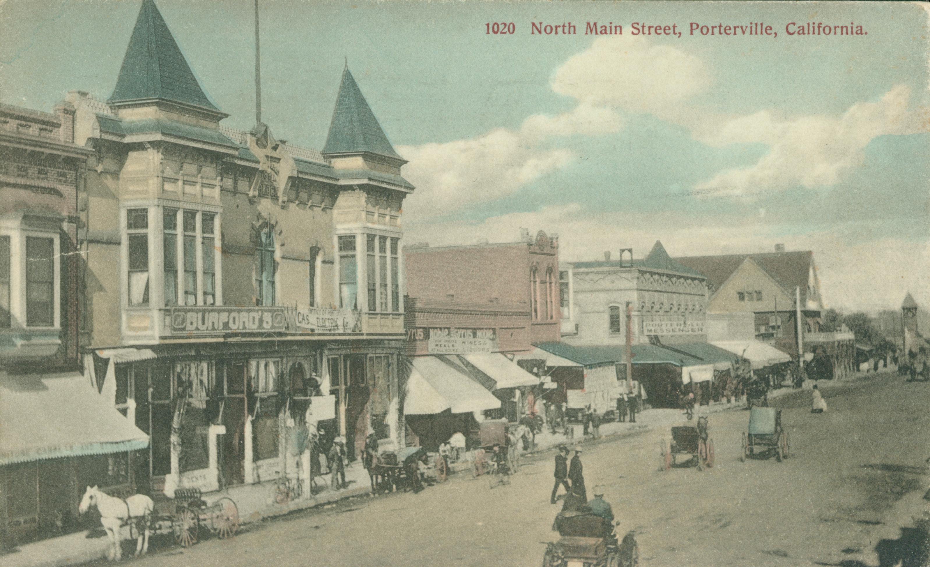 Shows Main Street in Porterville lined with buildings, with several cars and carriages in the road